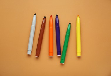 Photo of Different colorful markers on light brown background, flat lay