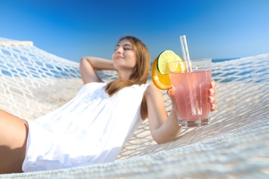 Photo of Young woman with refreshing cocktail relaxing in hammock outdoors, focus on hand