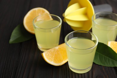 Photo of Tasty limoncello liqueur, lemon and green leaves on dark wooden table, closeup