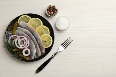 Photo of Salted herring fillets served with onion rings, pickles, dill and lemon on light beige wooden table, flat lay. Space for text