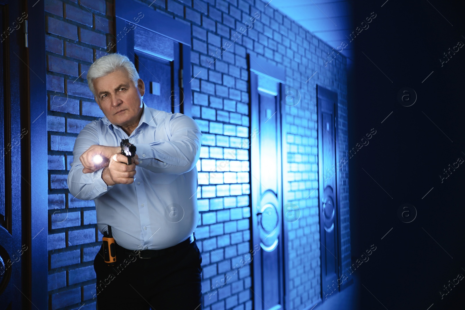 Photo of Professional security guard with gun and flashlight checking dark hallway