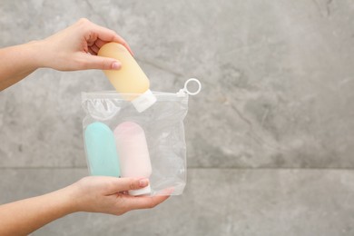 Photo of Woman packing cosmetic travel kit near grey wall closeup and space for text. Bath accessories