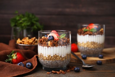 Photo of Tasty granola with berries, yogurt and chia seeds in glass on wooden table