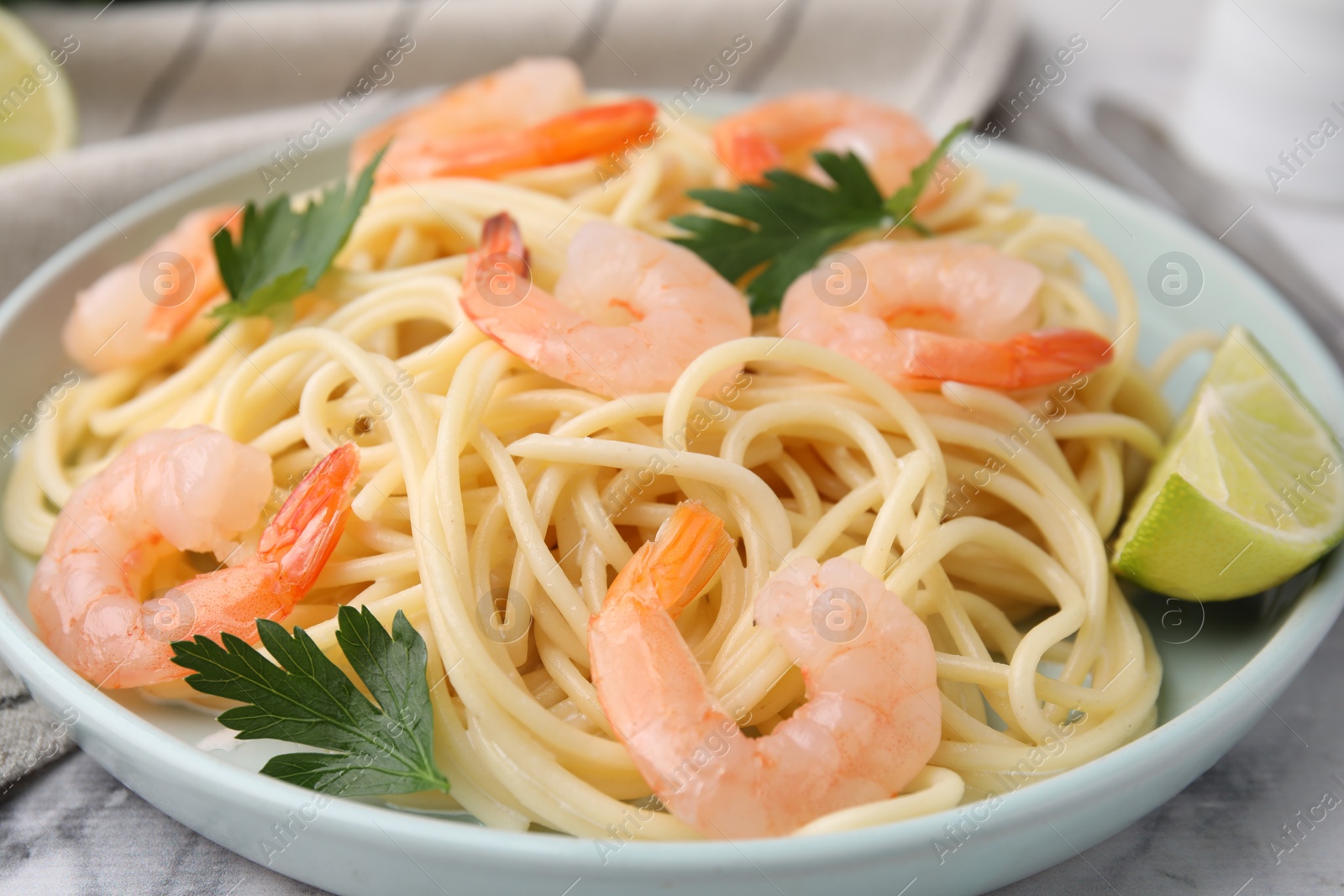 Photo of Tasty spaghetti with shrimps, lime and parsley on table, closeup