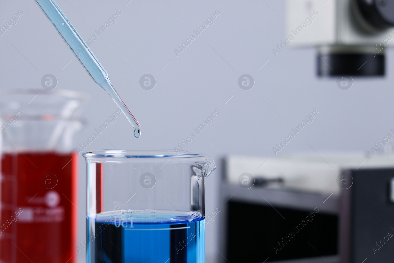 Photo of Dripping liquid from pipette into beaker in laboratory, closeup. Space for text