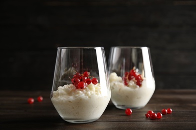 Photo of Creamy rice pudding with red currant in glasses and berries on wooden table