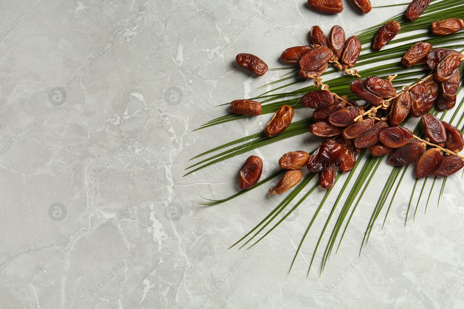 Photo of Tasty sweet dried dates and palm leaf on light table, flat lay. Space for text