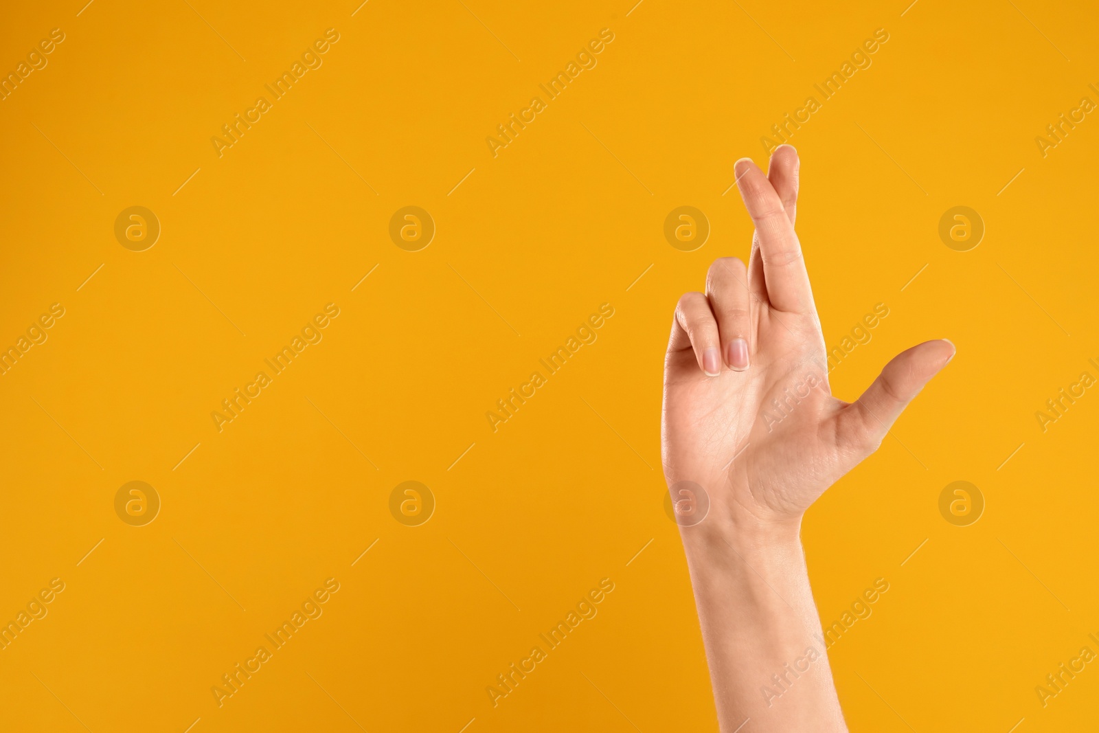 Photo of Woman with crossed fingers and space for text on yellow background, closeup. Superstition concept