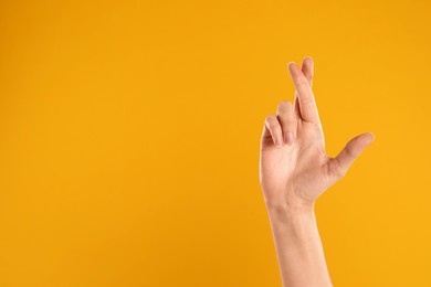 Photo of Woman with crossed fingers and space for text on yellow background, closeup. Superstition concept