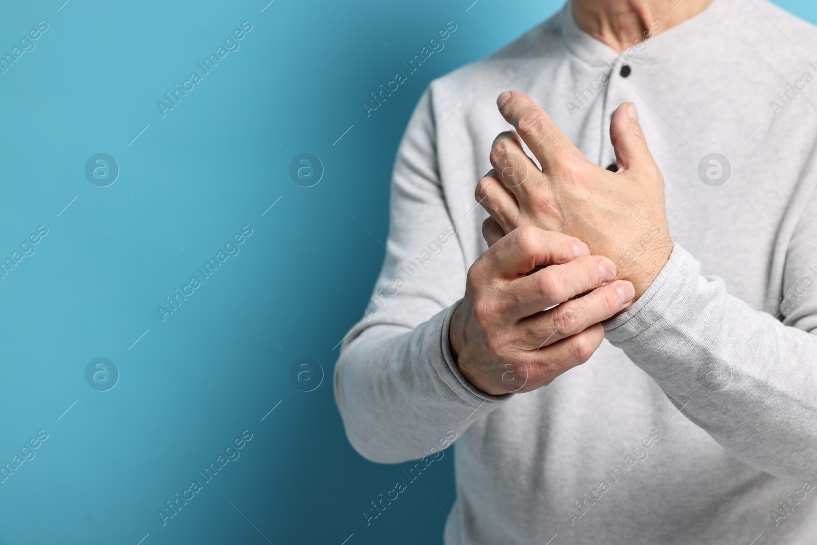 Photo of Arthritis symptoms. Man suffering from pain in hand on light blue background, closeup. Space for text