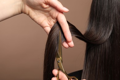 Photo of Hairdresser cutting client's hair with scissors on light brown background, closeup