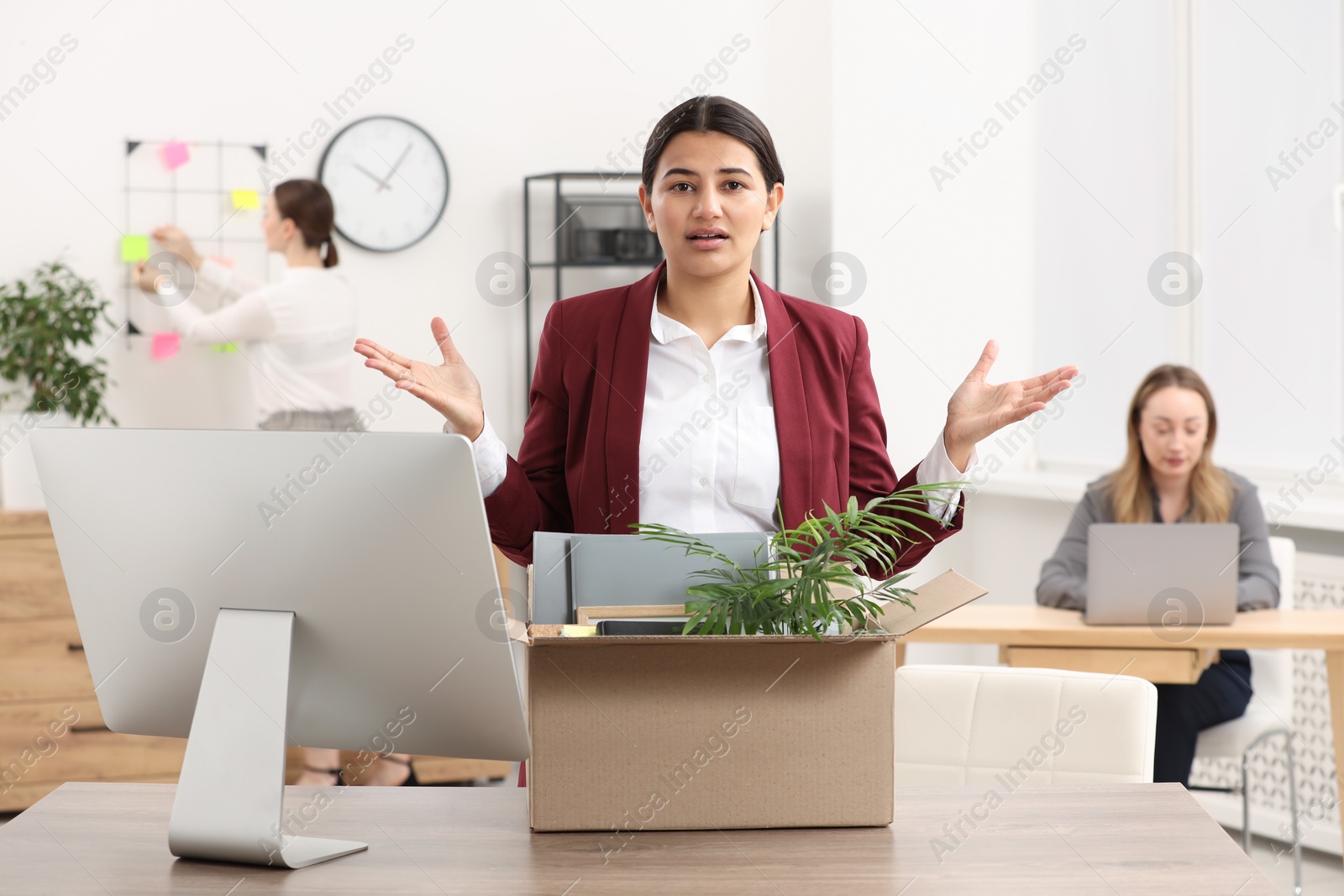 Photo of Unemployment problem. Woman with box of personal belongings at table in office