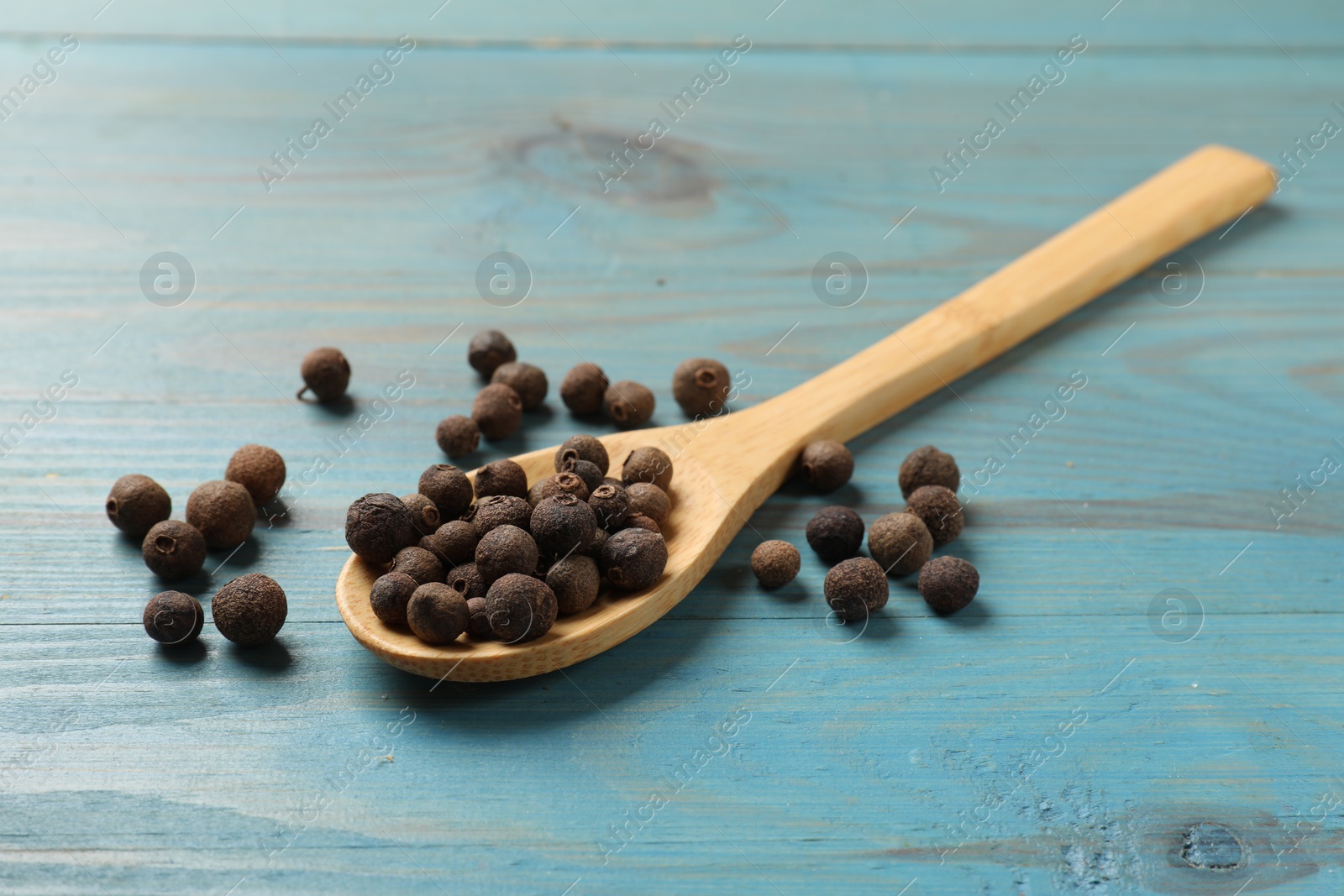 Photo of Aromatic allspice pepper grains and spoon on light blue wooden table