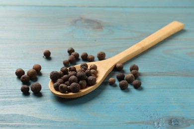 Photo of Aromatic allspice pepper grains and spoon on light blue wooden table