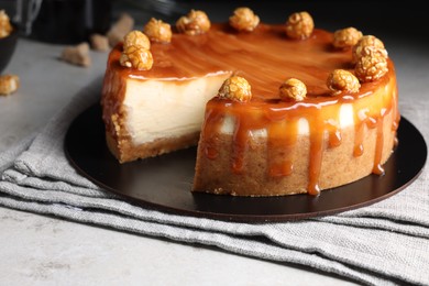 Photo of Sliced delicious cheesecake with caramel and popcorn on light grey table, closeup
