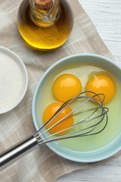 Whisking eggs in bowl on white wooden table, top view