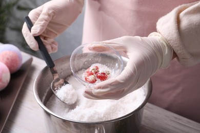 Photo of Woman in gloves making bath bomb at wooden table indoors, closeup
