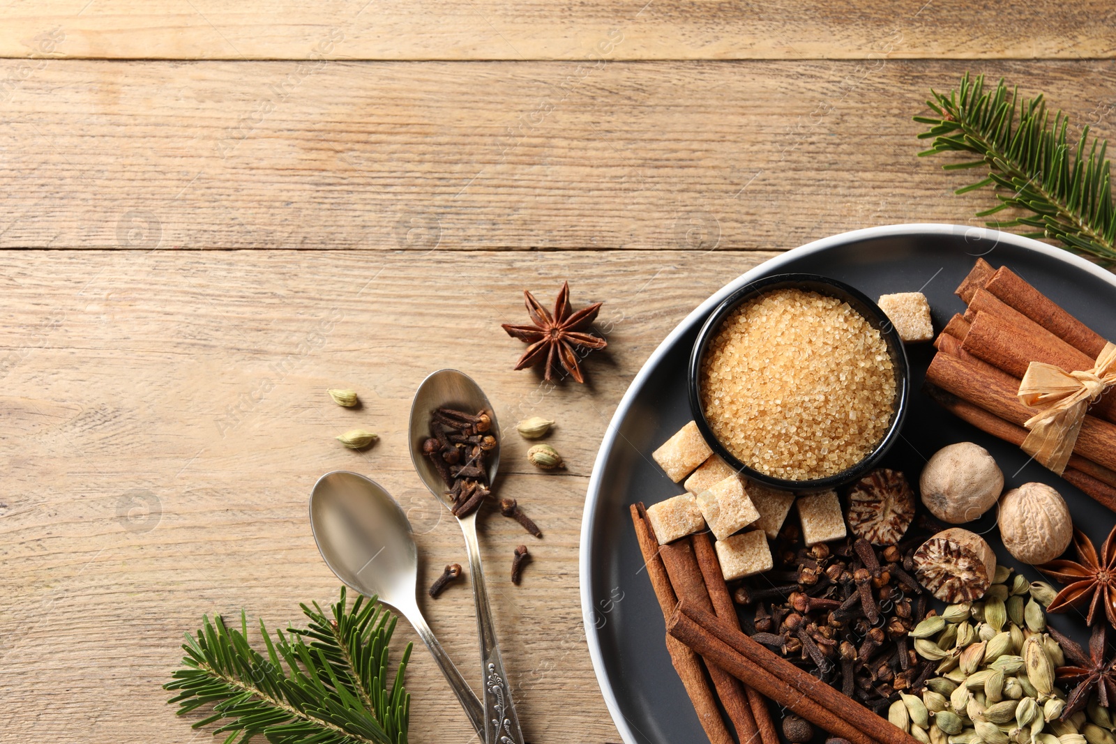 Photo of Plate with different aromatic spices, spoons and fir branches on wooden table, flat lay. Space for text