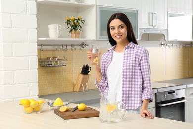 Photo of Beautiful young woman with lemon water in kitchen