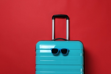 Photo of Stylish suitcase with sunglasses on color background, top view