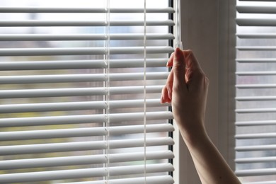 Photo of Woman opening white blinds at home, closeup