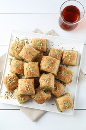 Photo of Delicious fresh baklava with chopped nuts and tea on white wooden table, top view. Eastern sweets