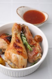 Photo of Marinade, roasted chicken drumsticks, rosemary and tomatoes on white tiled table, closeup