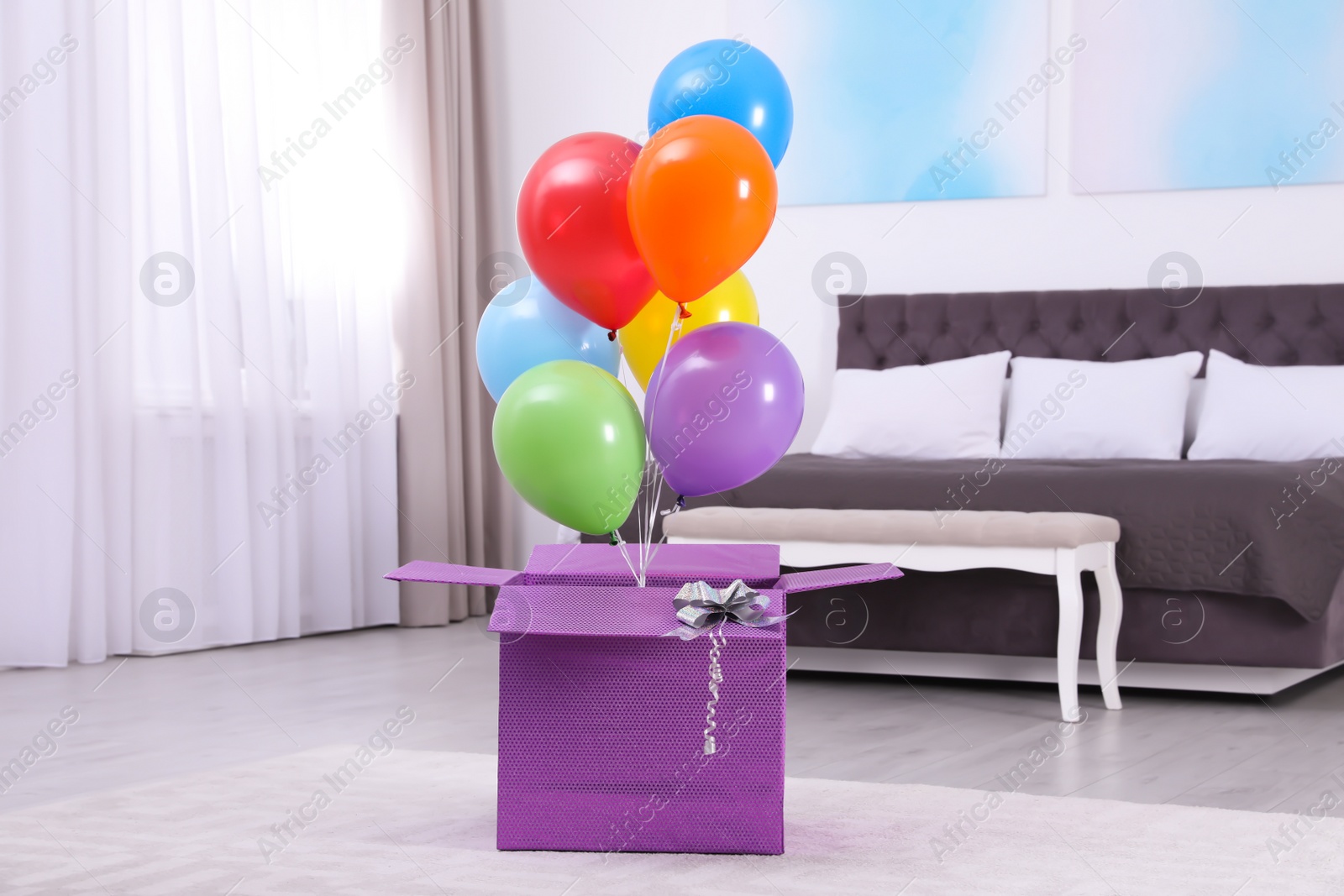 Photo of Gift box with bright air balloons in modern bedroom