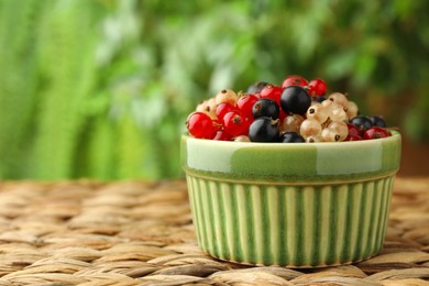 Photo of Different fresh ripe currants in bowl on wicker surface outdoors, closeup. Space for text