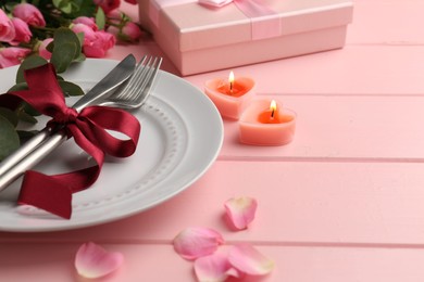Photo of Romantic place setting with roses and candles on pink table, closeup. Space for text