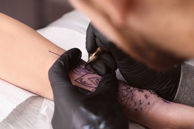 Photo of Professional artist making tattoo on hand at table, closeup