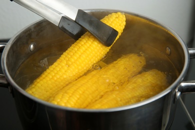 Taking fresh corn cob from pot with hot water on stove