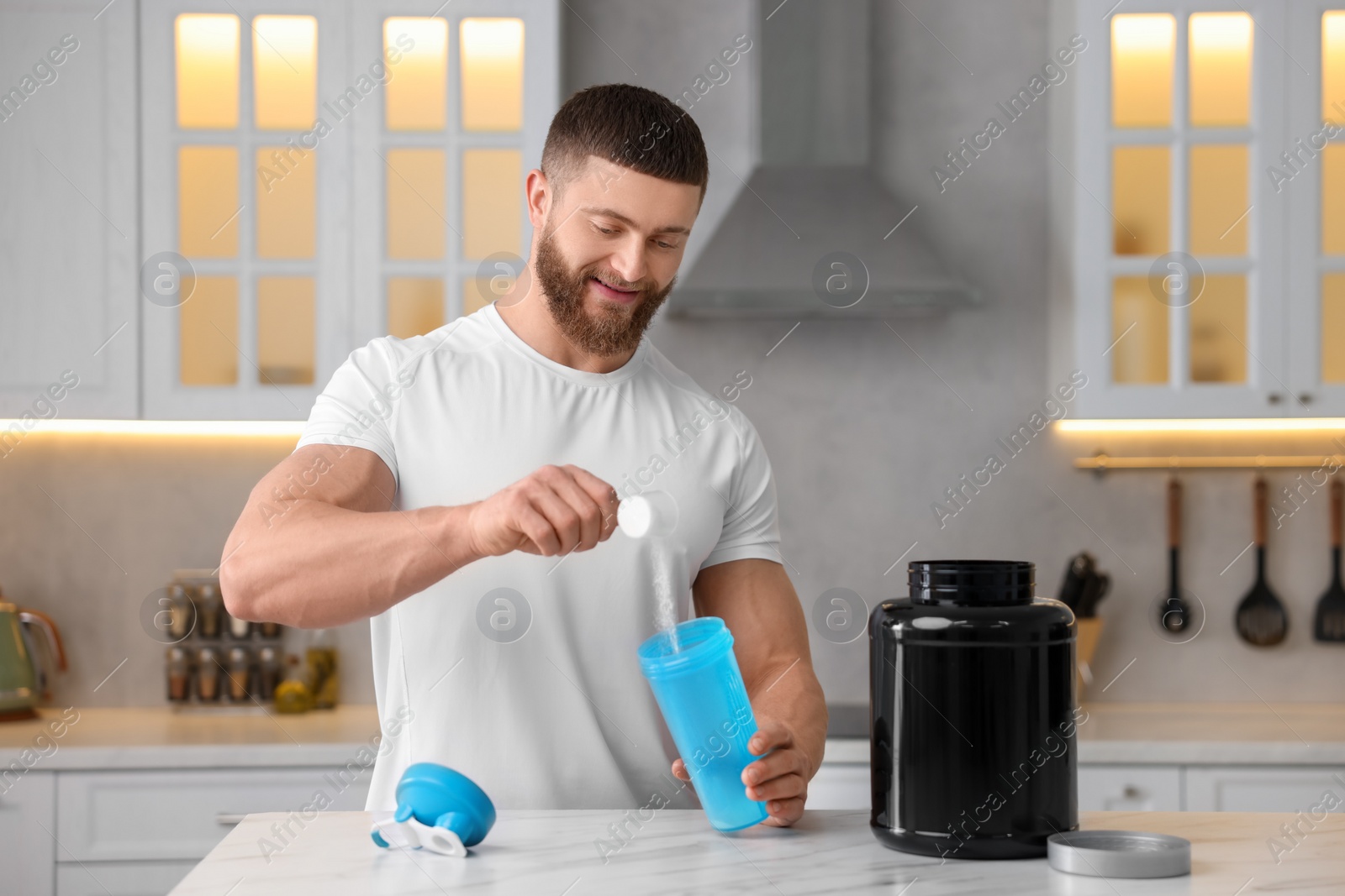 Photo of Young man making protein shake at white marble table in kitchen