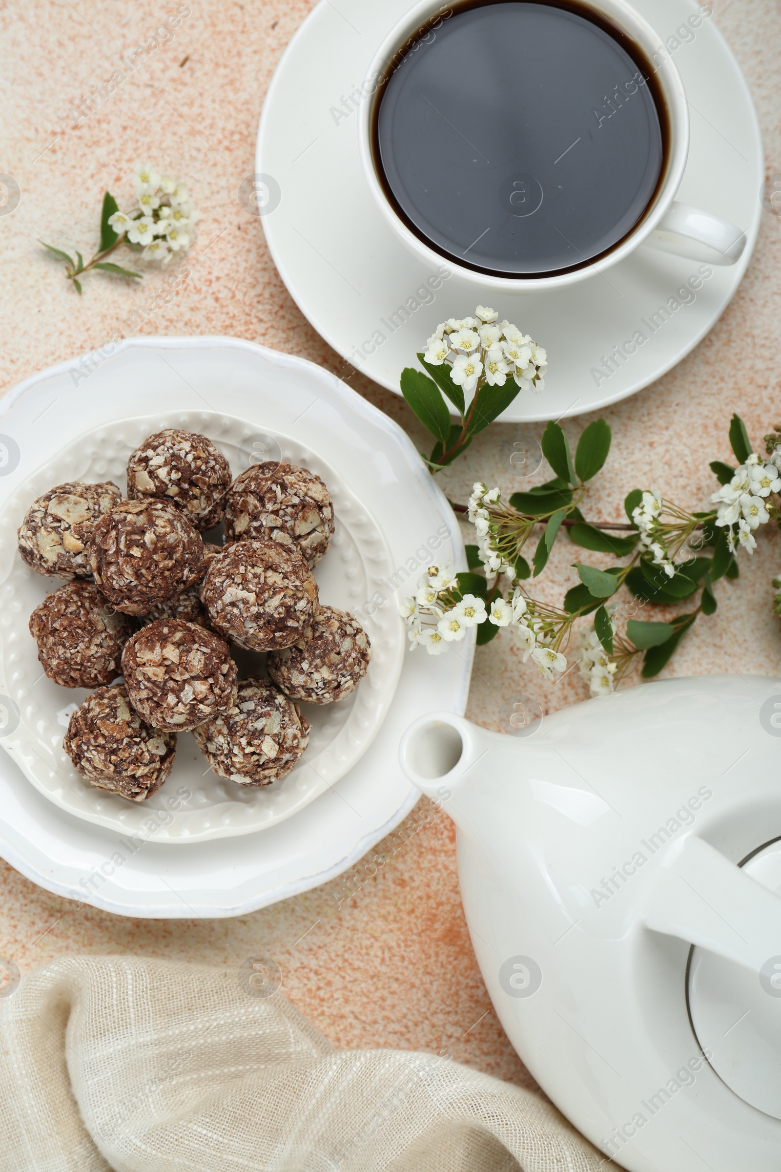 Photo of Delicious chocolate candies, cup of hot drink, teapot and blooming branch on beige table, flat lay