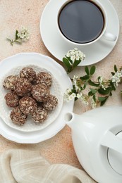 Photo of Delicious chocolate candies, cup of hot drink, teapot and blooming branch on beige table, flat lay