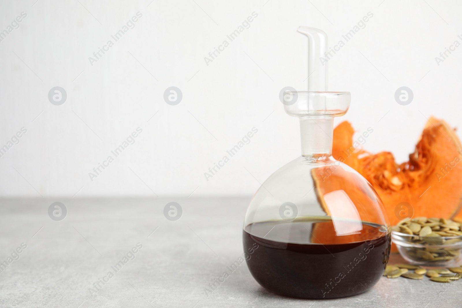 Photo of Laboratory glassware of oil with cut pumpkin and seeds on light grey table. Space for text