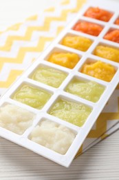 Photo of Different purees in ice cube tray on white wooden table, closeup. Ready for freezing