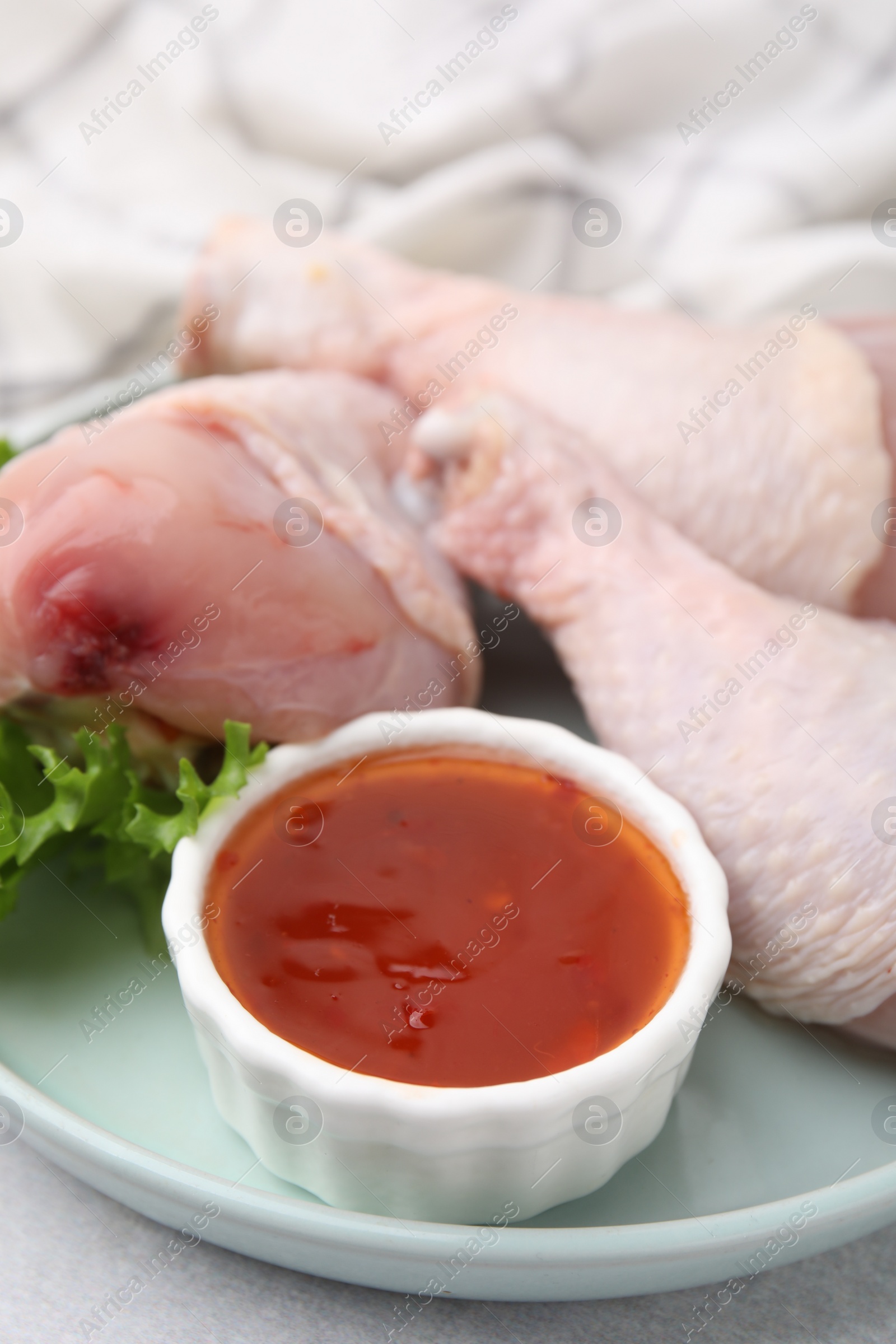 Photo of Fresh marinade, raw chicken drumsticks and lettuce on light table, closeup