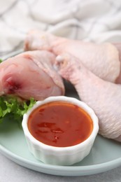 Fresh marinade, raw chicken drumsticks and lettuce on light table, closeup