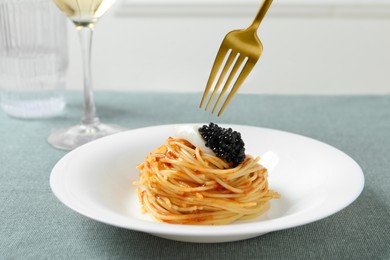 Photo of Eating tasty spaghetti with tomato sauce and black caviar at table, closeup. Exquisite presentation of pasta dish
