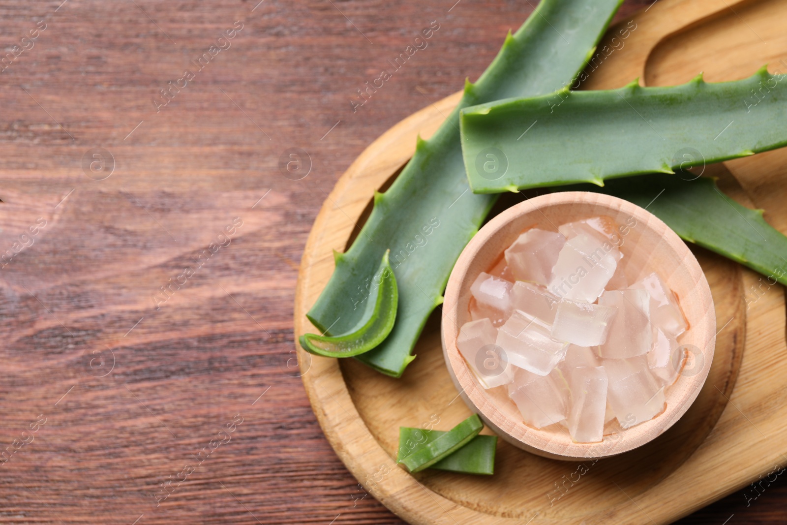 Photo of Aloe vera gel and slices of plant on wooden table, flat lay. Space for text