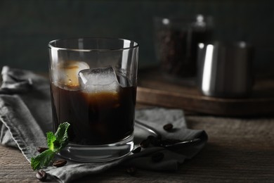 Photo of Glass of delicious iced coffee, mint and beans on wooden table, space for text