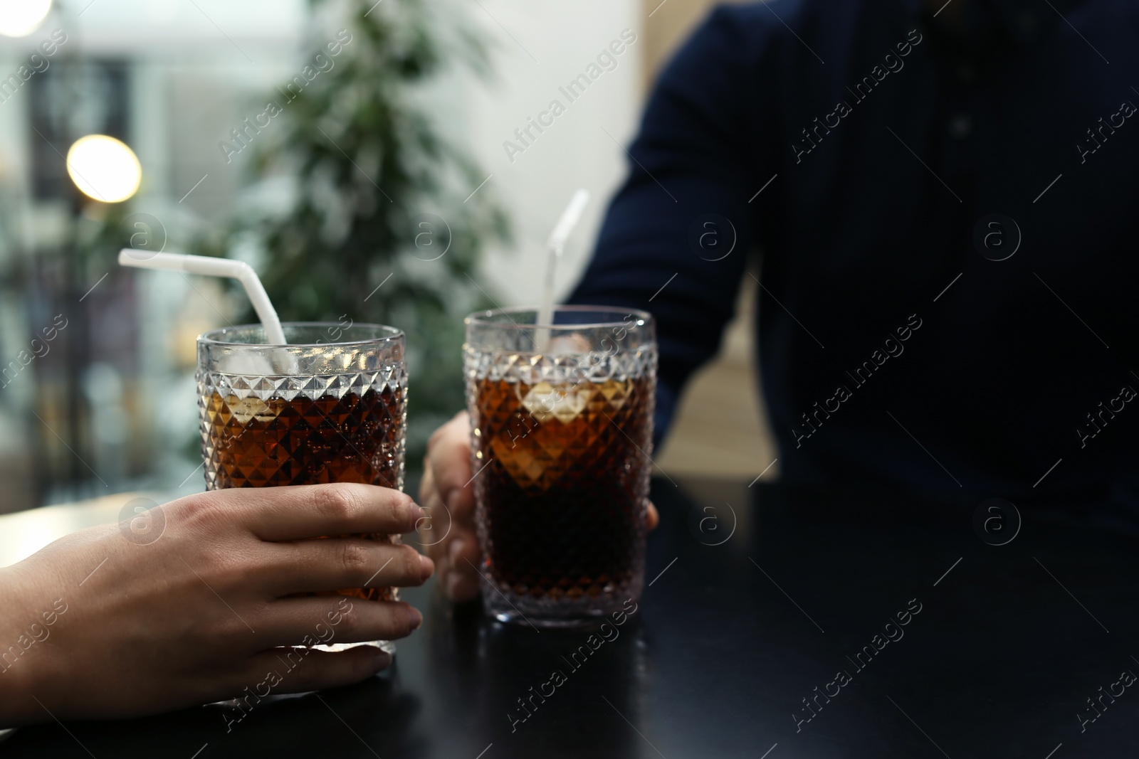 Photo of Couple with glasses of cold cola at table in cafe, closeup