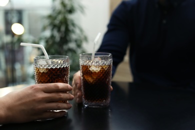 Couple with glasses of cold cola at table in cafe, closeup