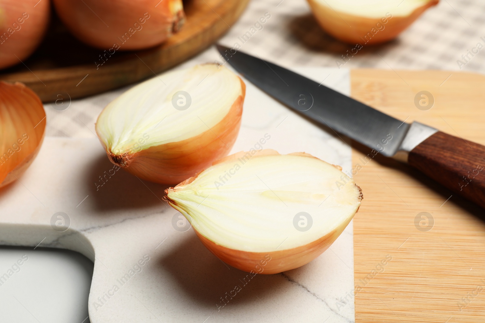 Photo of Whole and cut onions with knife on white table, closeup