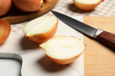 Whole and cut onions with knife on white table, closeup