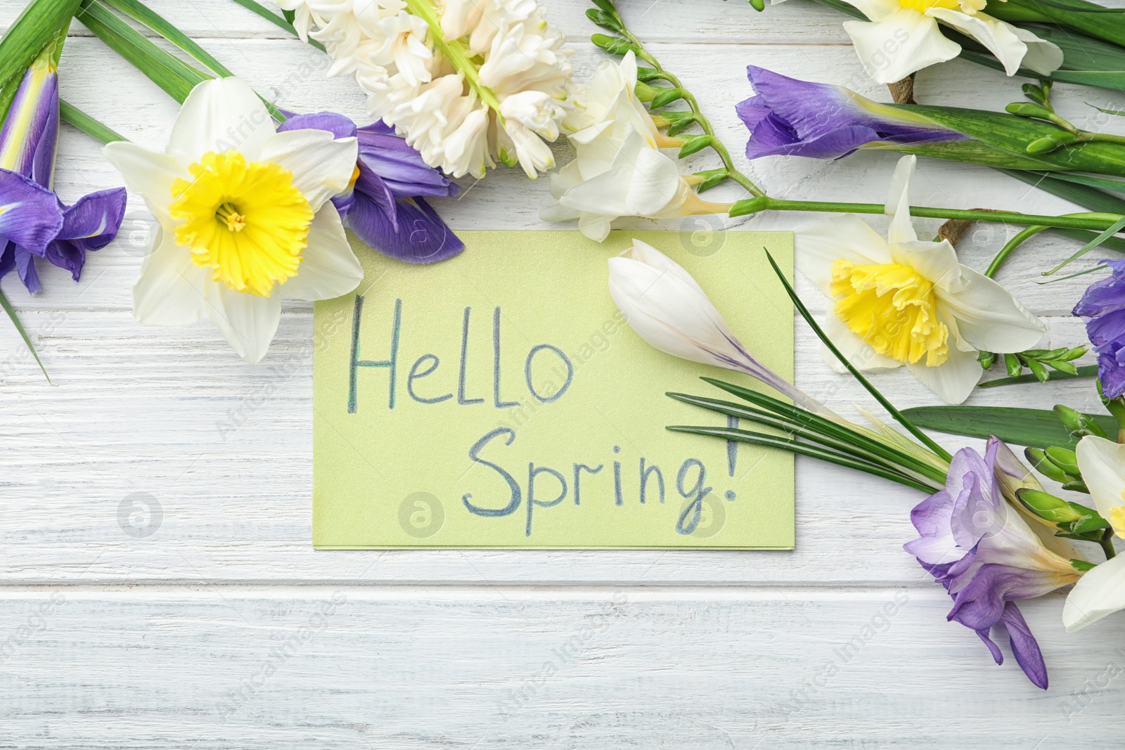 Photo of Card with words HELLO SPRING and fresh flowers on white wooden table, flat lay