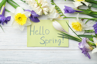 Photo of Card with words HELLO SPRING and fresh flowers on white wooden table, flat lay