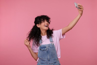 Beautiful young woman taking selfie on pink background