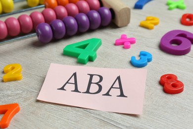 Photo of Paper sheet with abbreviation ABA (Applied behavior analysis), abacus and colorful numbers on white wooden table, closeup